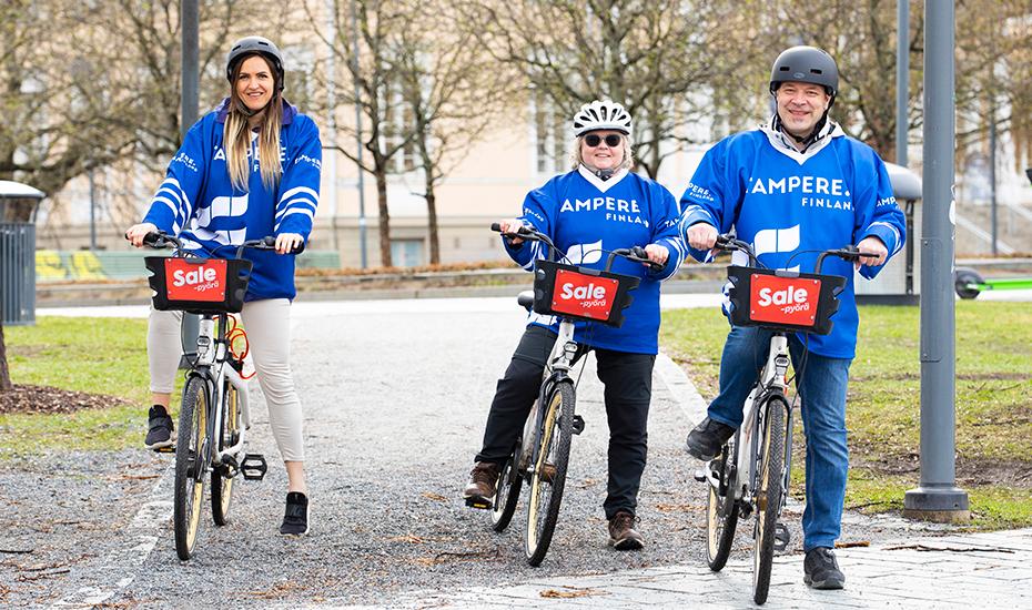 Kolme henkilöä kaupunkipyörillä kanssa. Ihmisillä on yllään Kiekon koti -paidat.