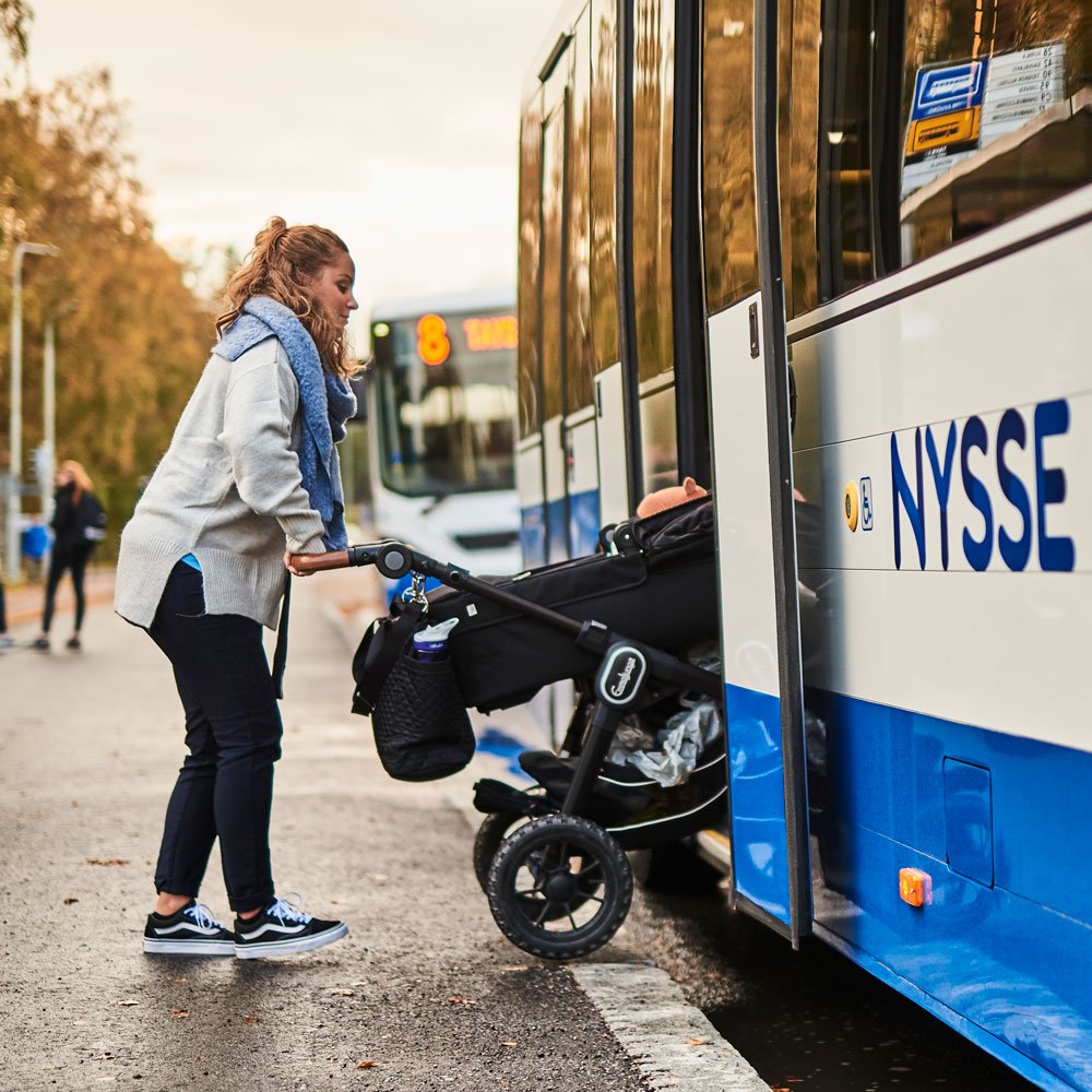 Äiti työntää vaunut bussin kyytiin vaunujen oikea kylki menosuuntaa kohti.