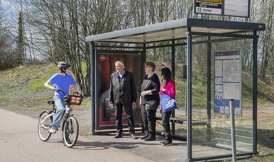 A cyclist passes a bus stop where people are standing.