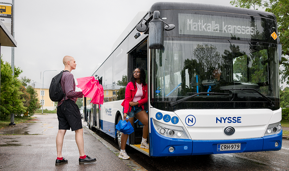 Kaksi henkilöä nousevat bussin kyytiin pysäkiltä. 