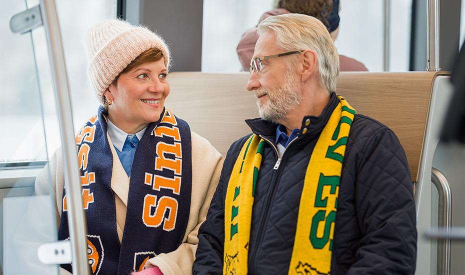 Kaksi matkustajaa ratikassa. Toisella on Tappara-kaulahuivi ja toisella Ilves-kaulahuivi.