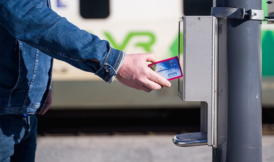 Matkustaja vahvistaa matkaoikeutensa asemalaiturin lipun lukijassa asettamalla matkakortin laitteen näytön alle.