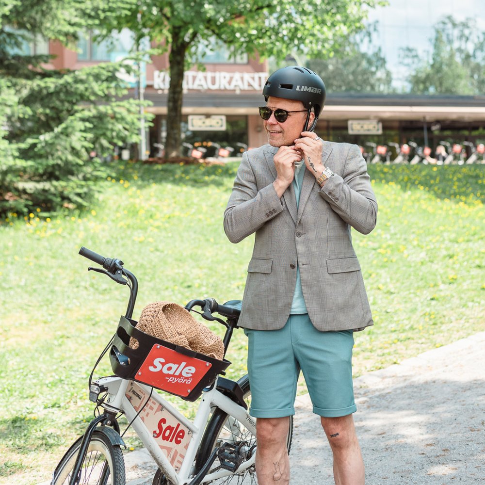 Henkilö kaupunkipyörän vieressä kiinnittää pyöräilykypärää. 