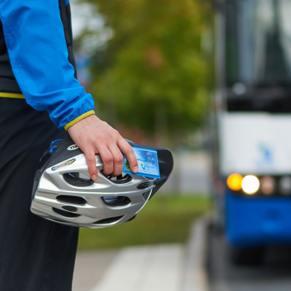 Passenger is waiting for a bus with a bike helmet on his hand.