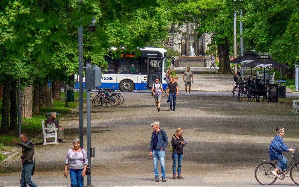 Bussi on matkalla kohti keskustaa Hämeenpuistossa. Terassi on avoinna ja ihmisiä on liikkeellä eri suuntiin kävellen ja polkupyörällä.