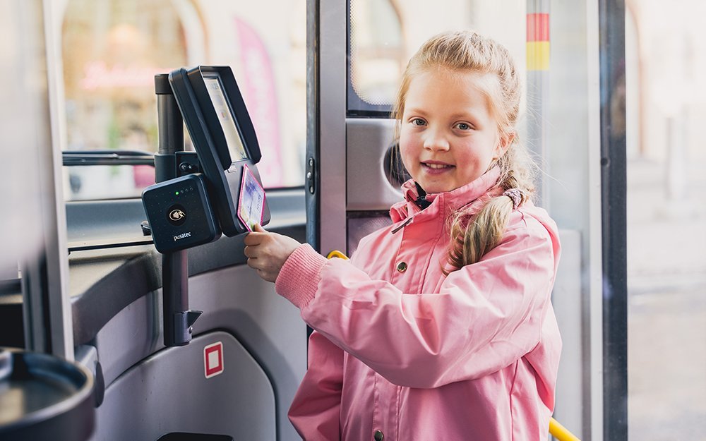 A little girl is showing her travel card to the card reader in the bus.