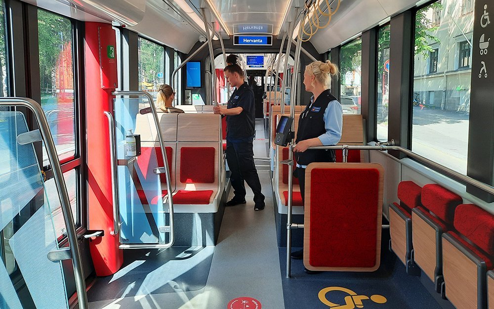A ticket inspector checks a passenger's ticket in a sunny tram.